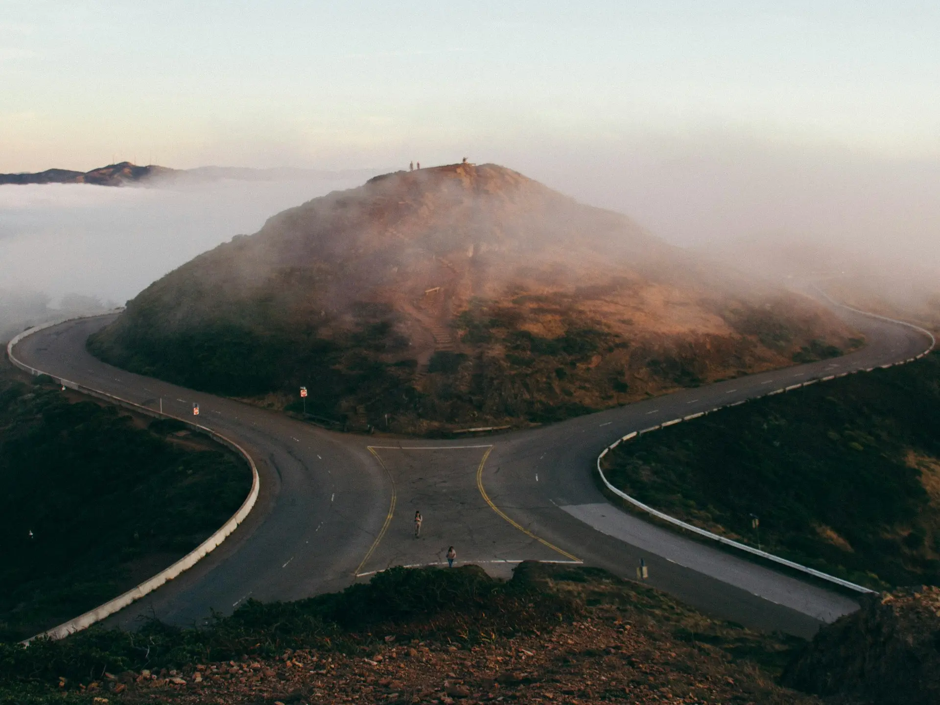 bird's-eye view photo of two people standing on gray concrete road in front of hill
