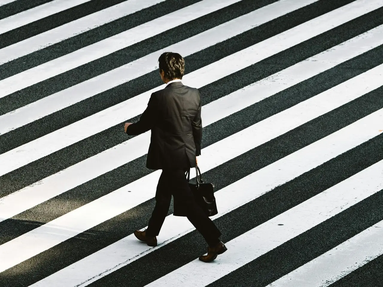 man in black formal suit jacket and pants carrying black bag while walking on pedestrian lane during daytime